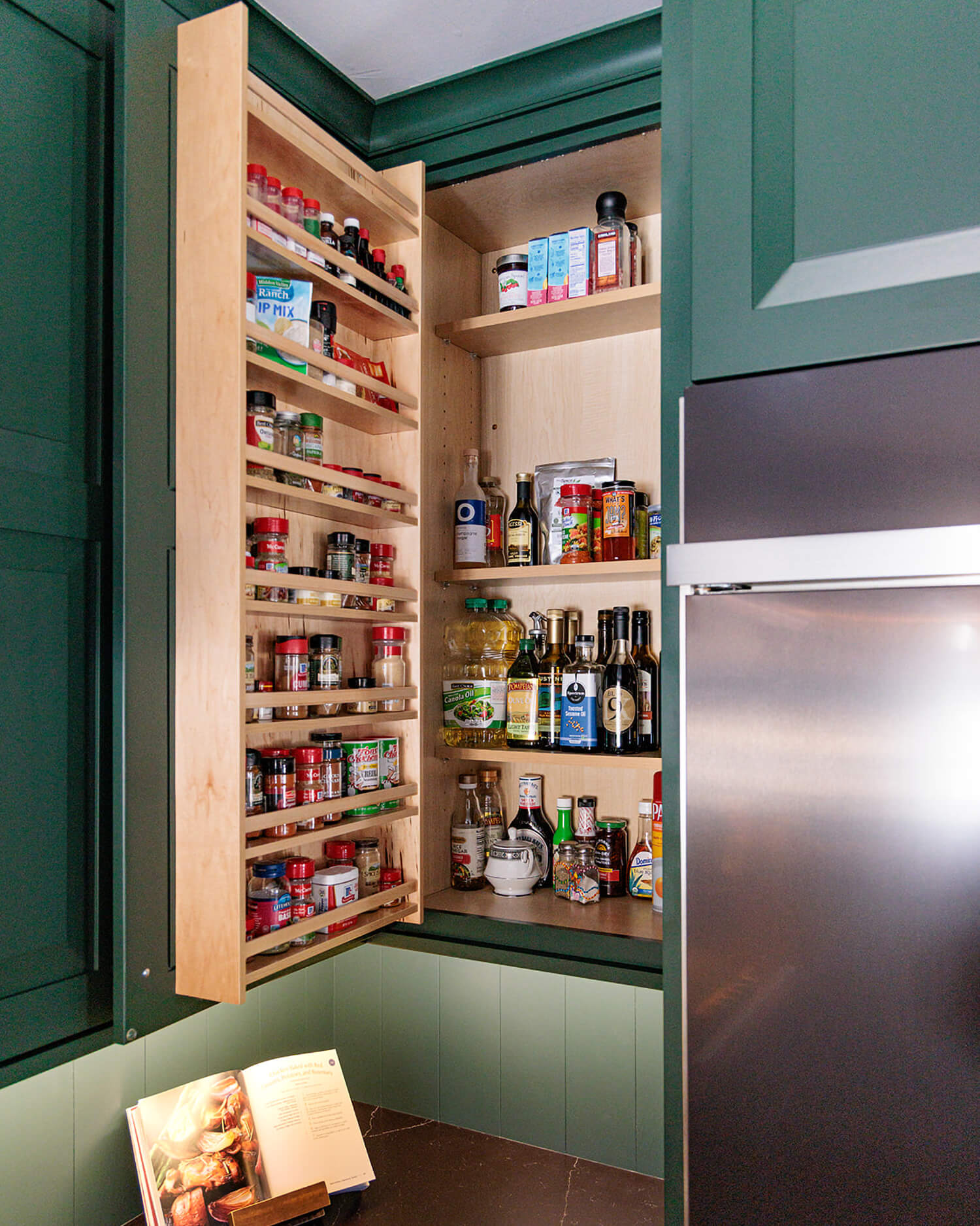 Dark forest green painted custom kitchen cabinets showcase a Cabinet Door Spice Rack for organized spice and pantry storage. This cabinet storage accessory keeps frequently used ingredients visible, accessible, and conveniently stored within one cabinet.