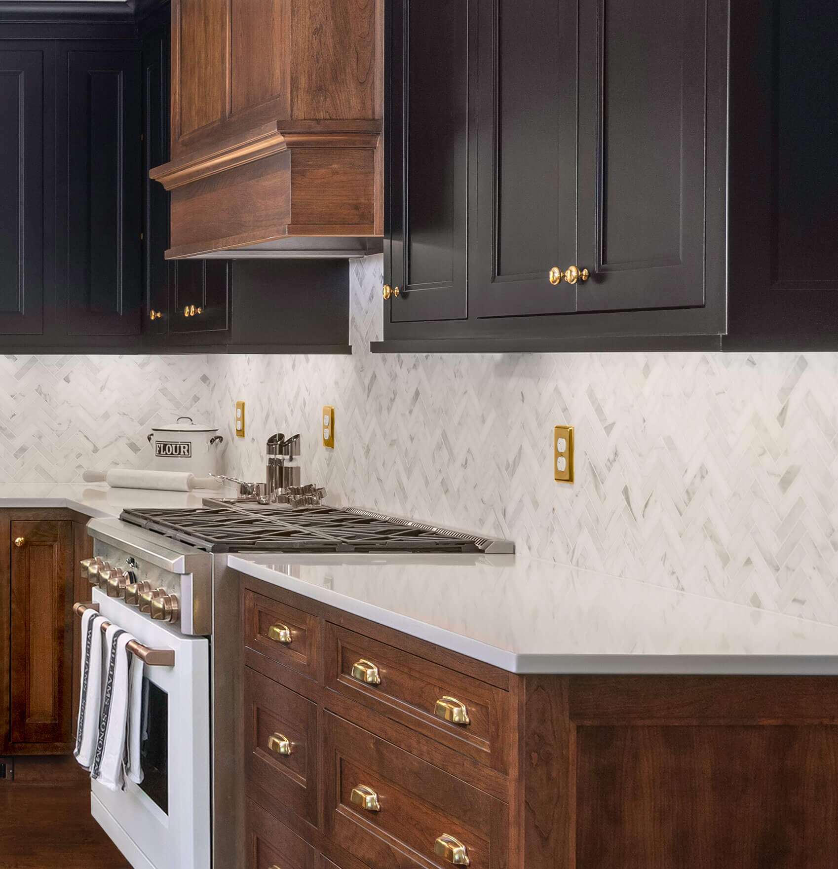 A two-toned kitchen with warm cherry wood cabinets and black painted cabinets. The integrated wood hood highlights the cooking area.