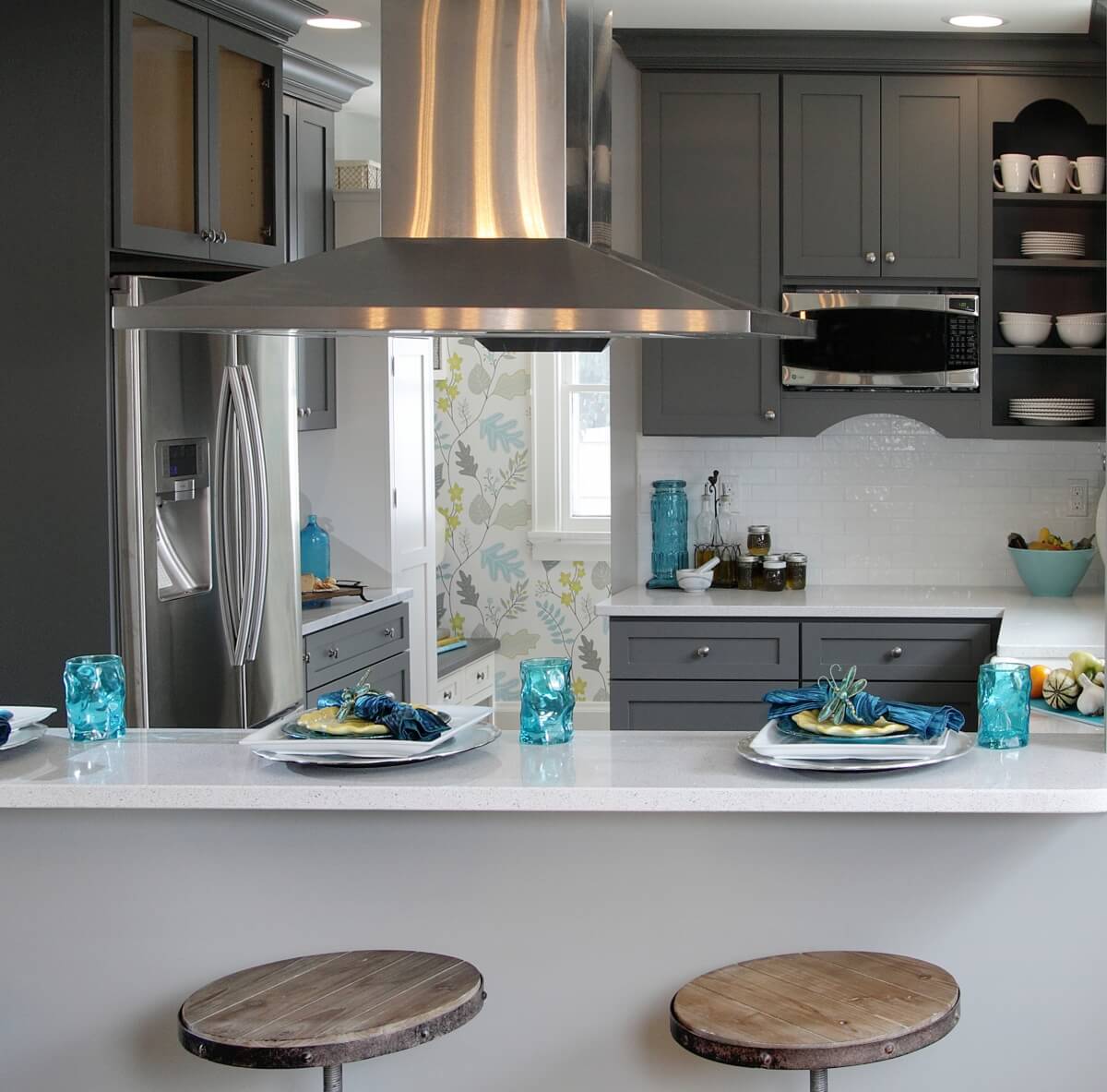 A dark gray painted kitchen with bold blue accents and brightly colored wallpaper.