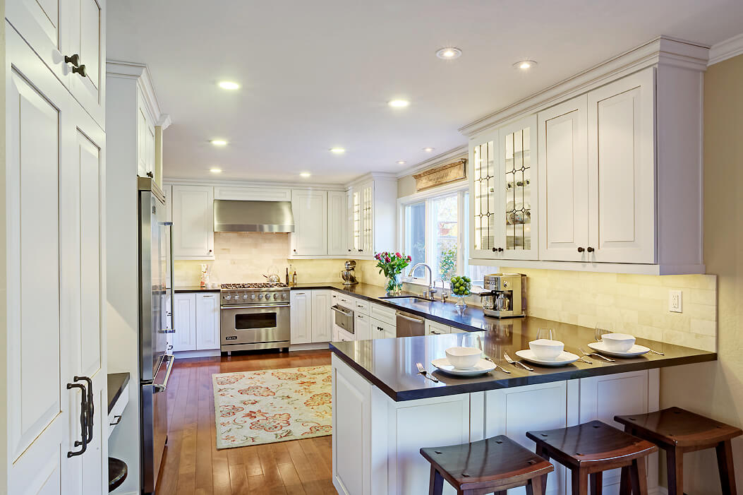 A G-shaped kitchen with white painted cabinets, dark countertops, and lots of cabinet storage.