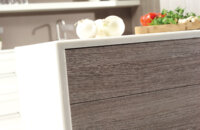 A close up of a contemporary kitchen island with a thin, white waterfall countertop and textured shiplap panels.