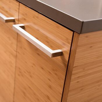 A detailed photo of a modern kitchen with bamboo veneer cabinets. The solid slab door style is sleek and stylish. The kitchen cabinets are shown with a full-access cosntruction method.