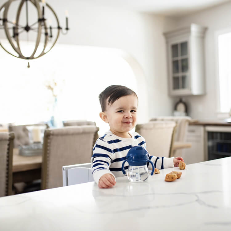 An adorable toddler sitting at a bar stool eating at a kitchen island with countertop height seating.