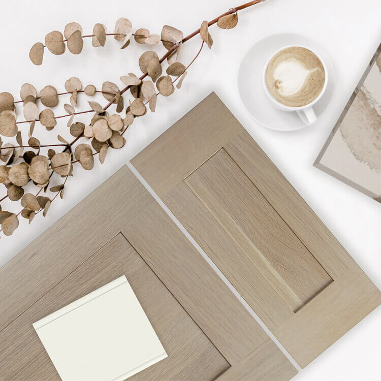 A shallow shaker cabinet door with a flat panel style is shown in this kitchen design mood board with a light stained finish on Quarter-sawn White Oak. A sample of an off-white painted finish with a natural hue lays on top of the door casually. Kitchen design trends lean towards natural inspired textures and paint colors.