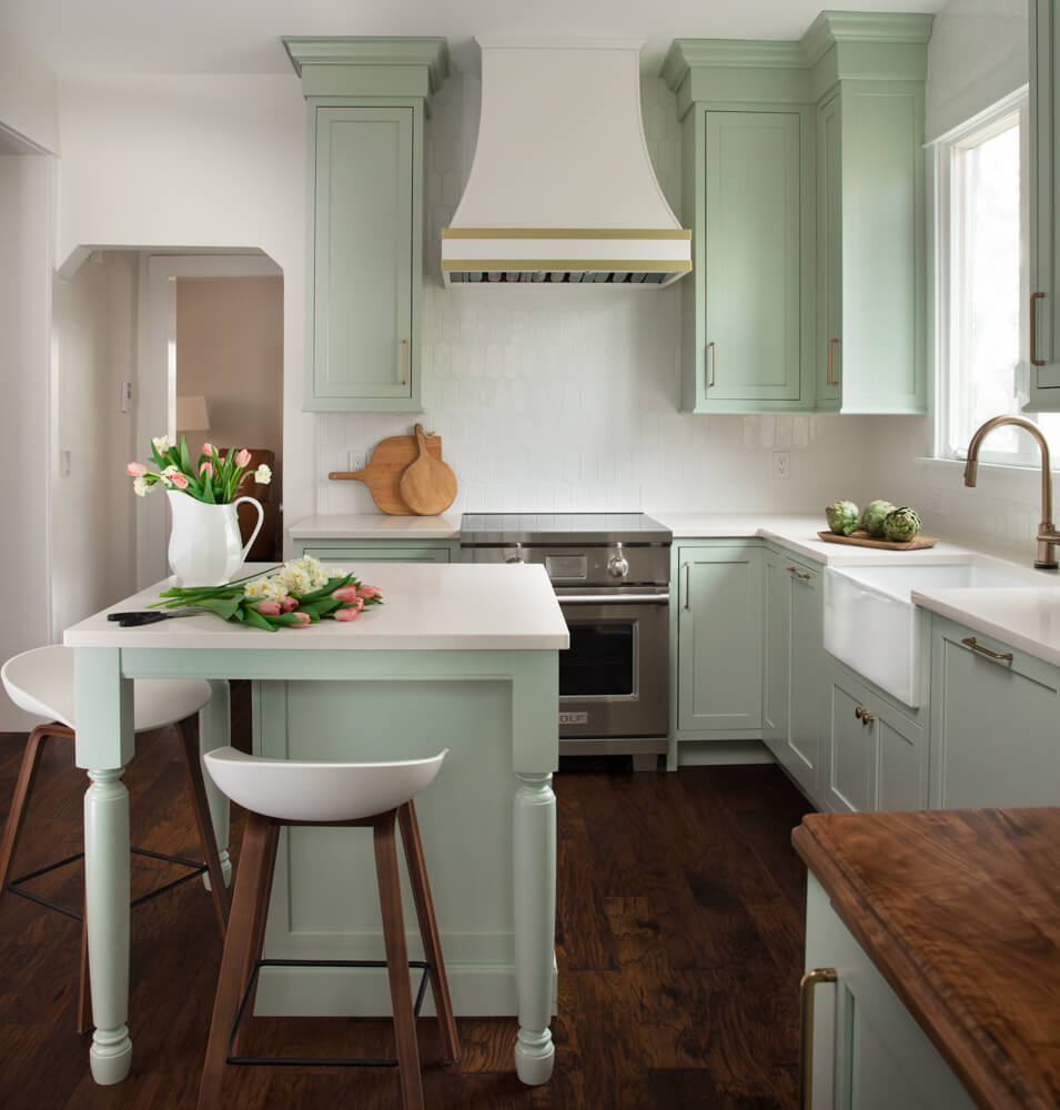 A colorful kitchen with minty green painted cabinets and a white range hood with gold hardware and accents.