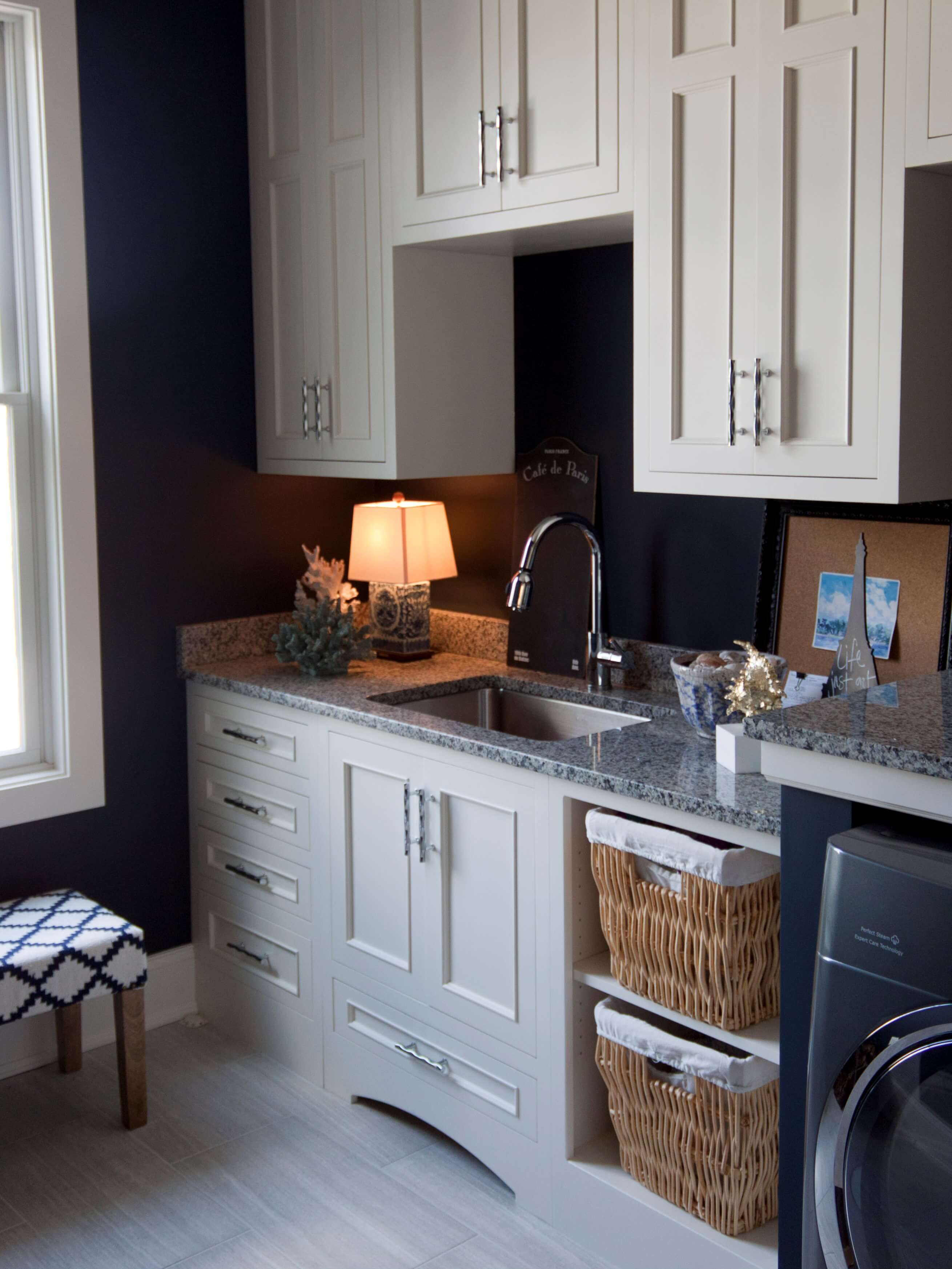 A pretty laundry room with white painted cabinets from Dura Supreme. and open storage for wicker laundry baskets.