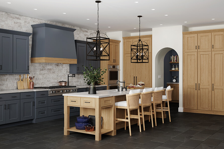 An old Englishh style kitchen design with deep dark navy blue painted cabinets contrasted by light stained cherry wood cabinets. The modern wood hood makes for a stunning focal point with the two toned paint and stain colors. The Dura Supreme kitchen island is a multi-functional workspace with countertop seating for four guests.