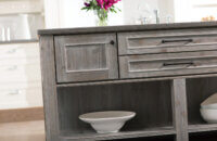 A light gray stained kitchen island with a weathered wood finish in a rustic Knotty Alder wood species.