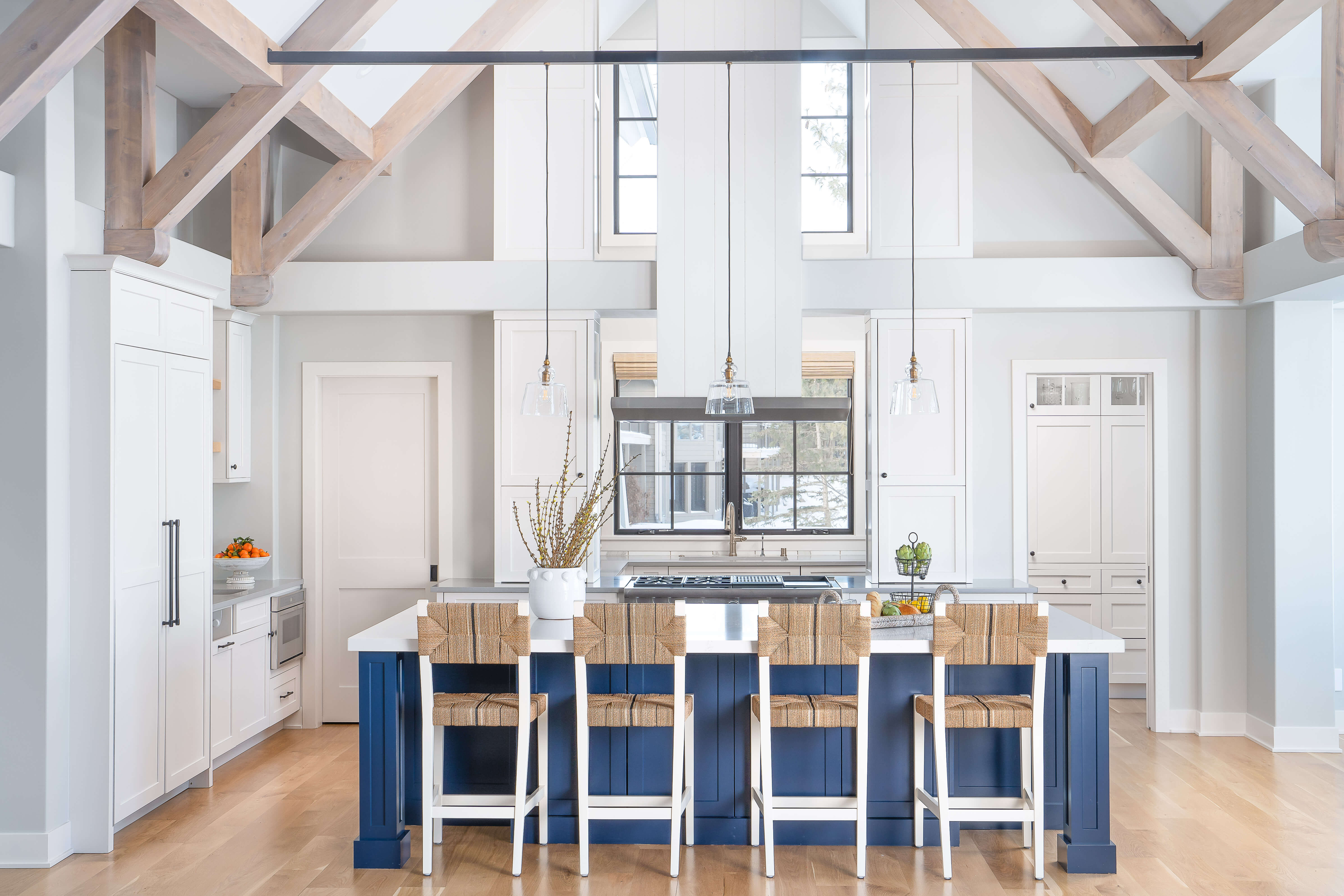 A bright white and blue modern farmhouse kitchen design with exposed ceiling beams, white painted cabinets, and blue kitchen island.
