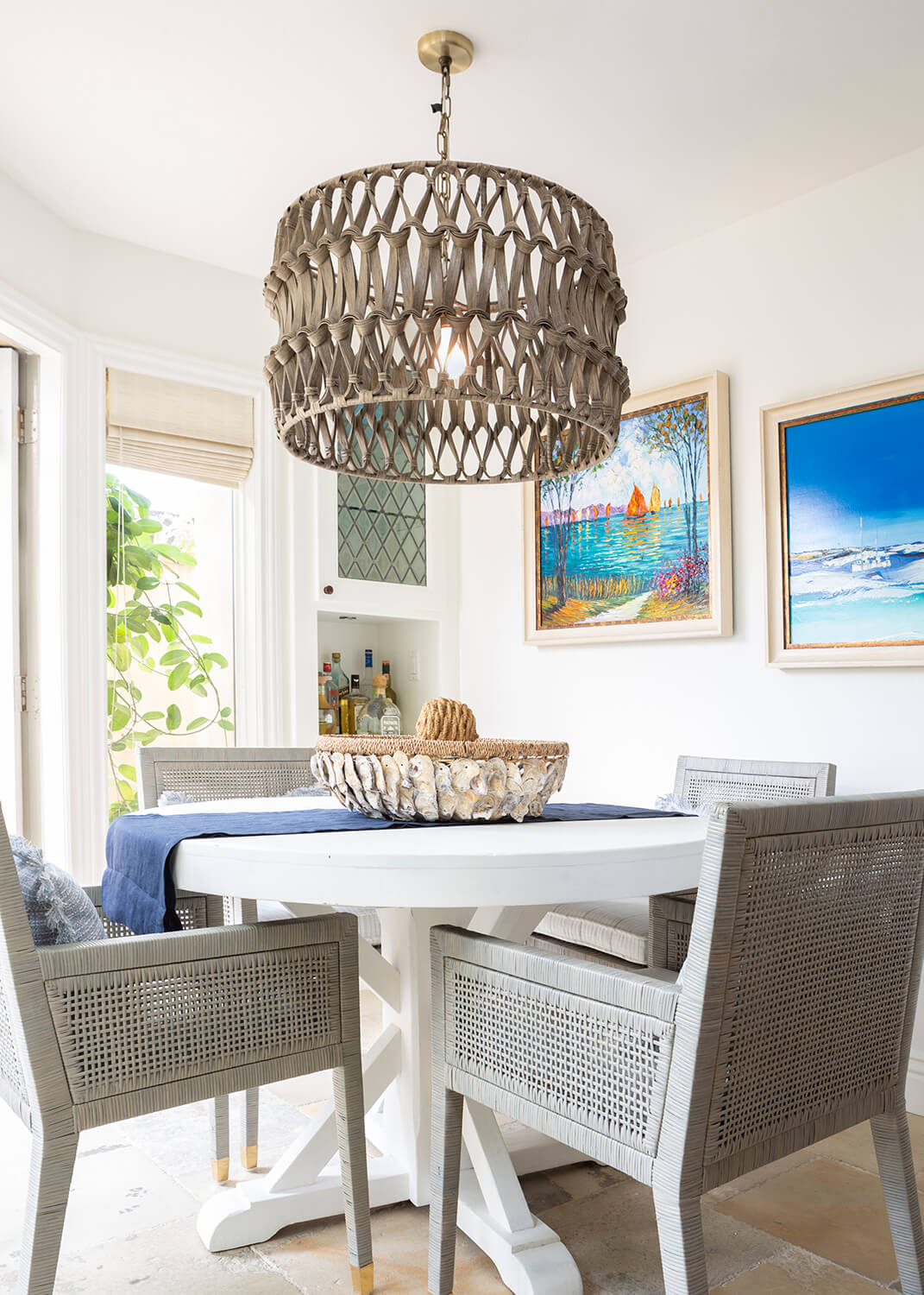 Coastal style interior design in a dining room with a large beach-inspired light.