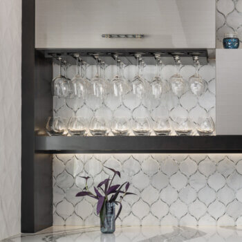 A collection of stemware and glassware displayed on a contemporary floating shelf and wine glass rack holder below a wall cabinet.
