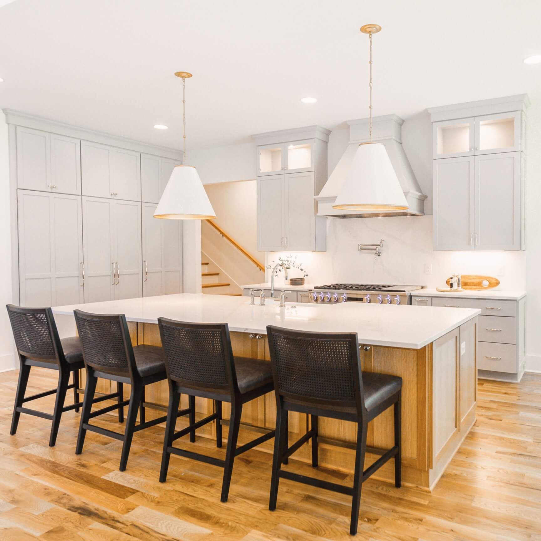 A white, bright, and cozy kitchen design with soft, off-white cabinetry with a contrasting kitchen island in a light stained wood finish.