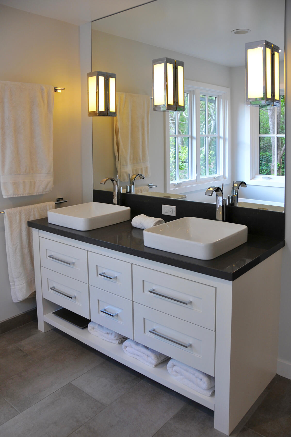 A white painted transitional styled furniture vanity with a shelf below the sink cabinets for extra towel storage.