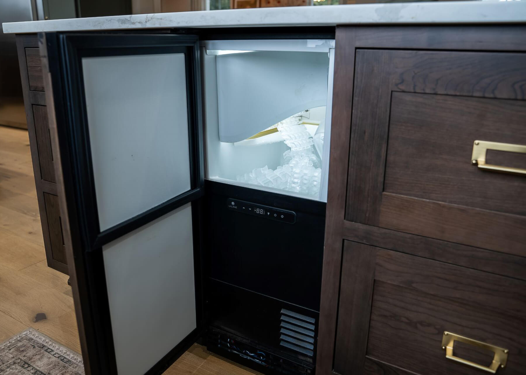 A hidden ice maker machine behind a beautiful cabinet door of a kitchen island designed for entertaining.