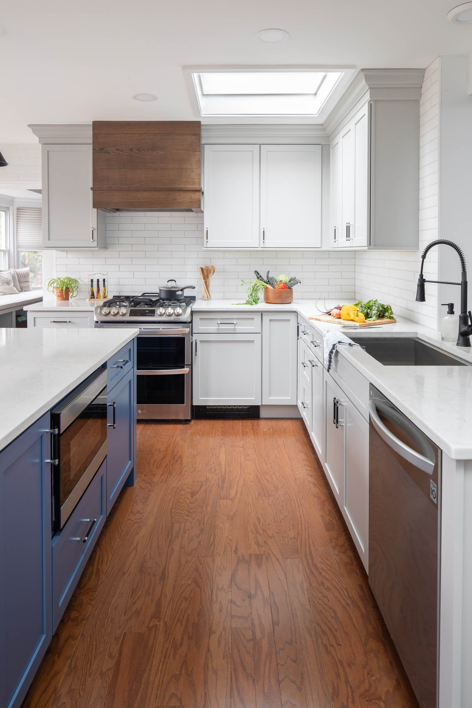 A straight on view of a three-toned kitchen featuring a Red Oak wood hood paired with a white paint for the perimeter cabinets and a light blue paint for the kitchen island.