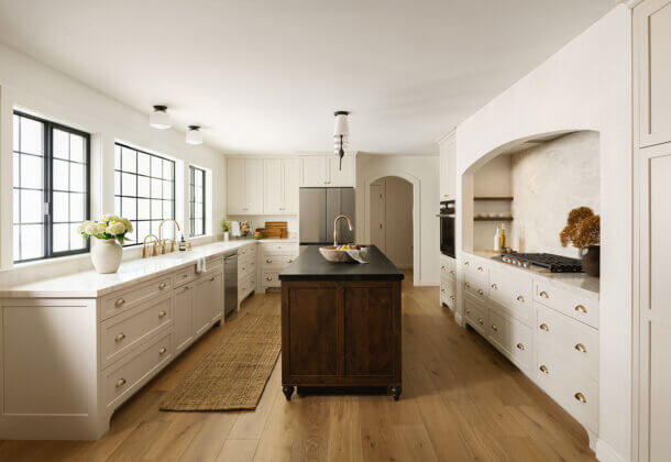 Custom kitchen cabinets in a bright, open kitchen featuring full-height cabinetry, expansive countertop workspace, a contrasting island, black-framed windows, and warm wood flooring that creates a clean, timeless design.