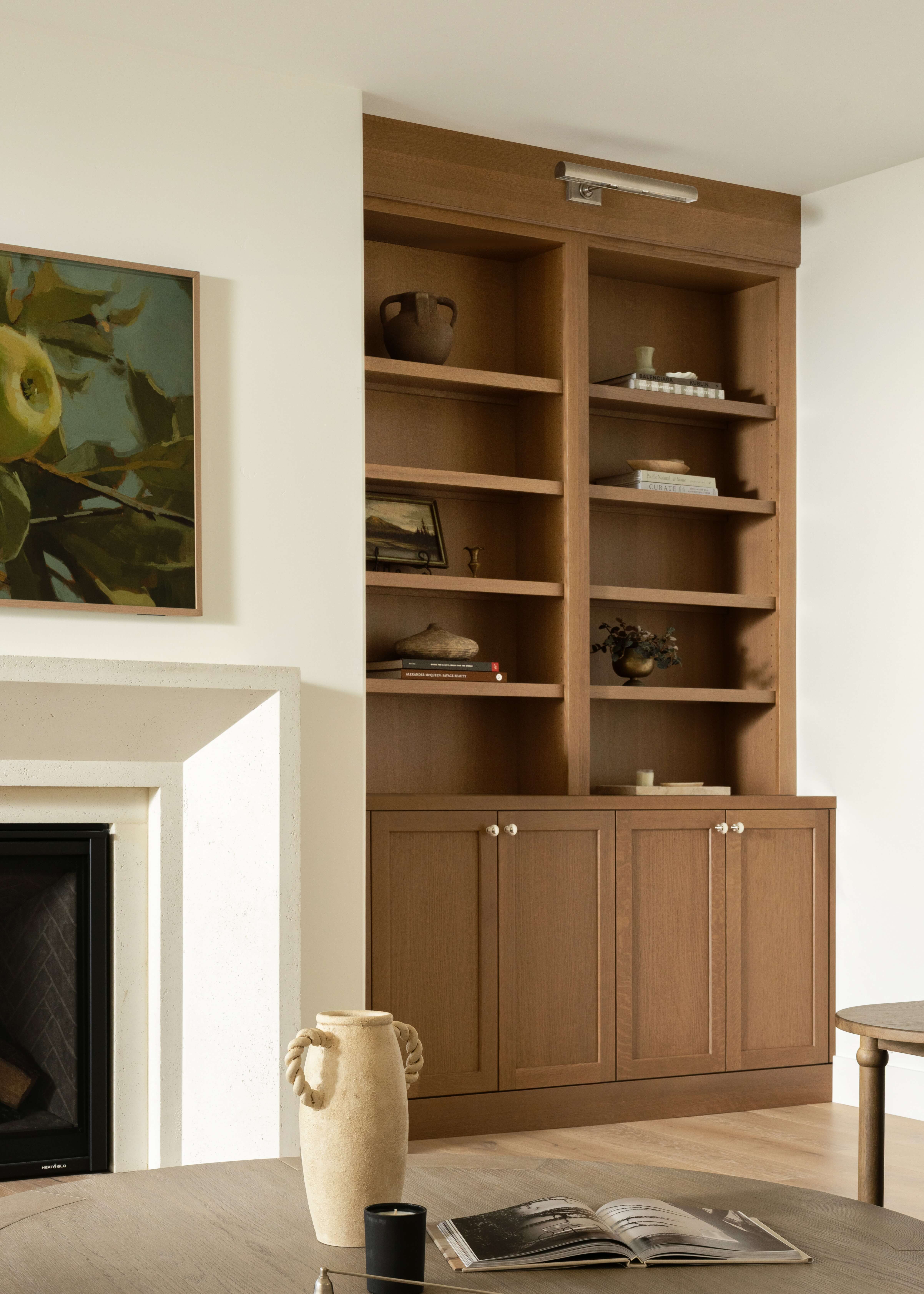Built in cabinets in a medium brown stained wood finish create a warm, furniture-inspired focal point with open bookshelves and concealed storage below. Gold cabinet hardware adds a refined touch while showcasing books, décor, and everyday essentials.